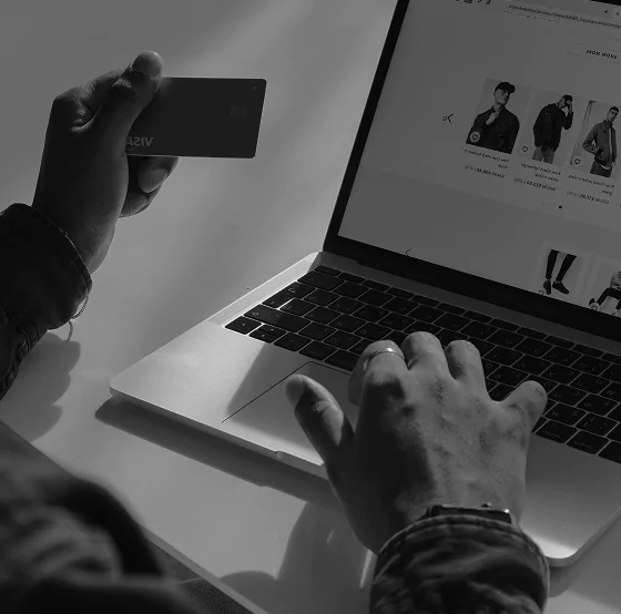 A person holding a credit card while using a laptop to browse an online clothing store, indicating online shopping or e-commerce activity.